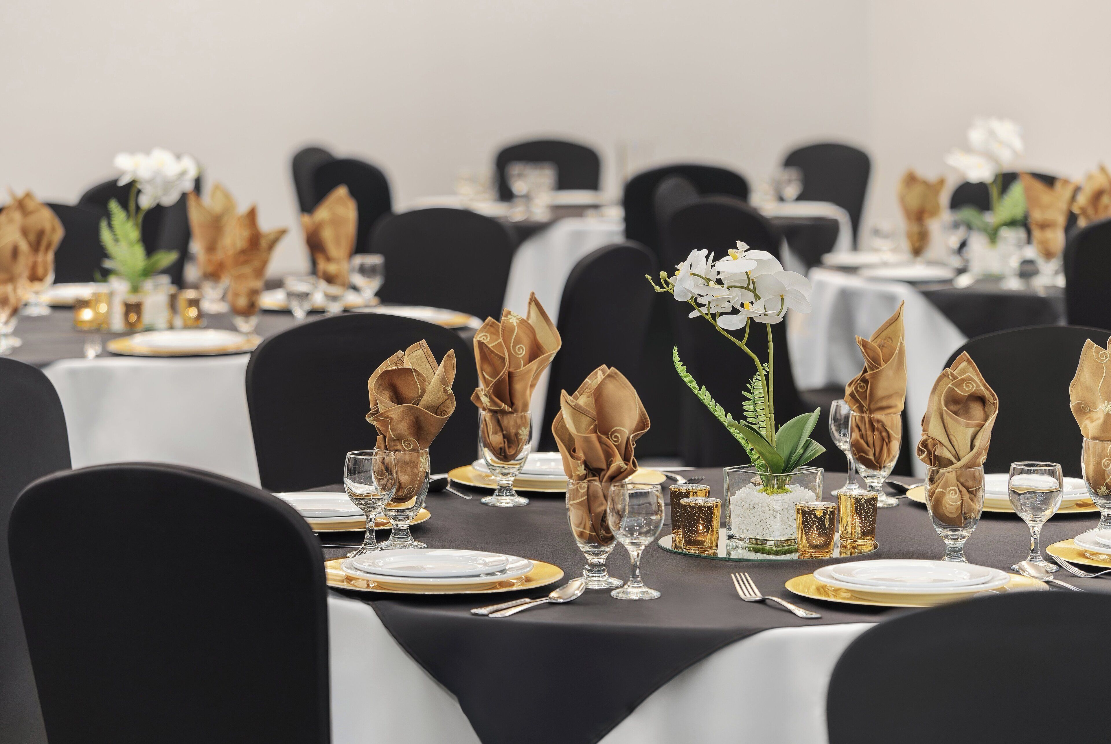 Taula de banquet posta amb serretes daurades, plats blancs i vetrereria transparent.