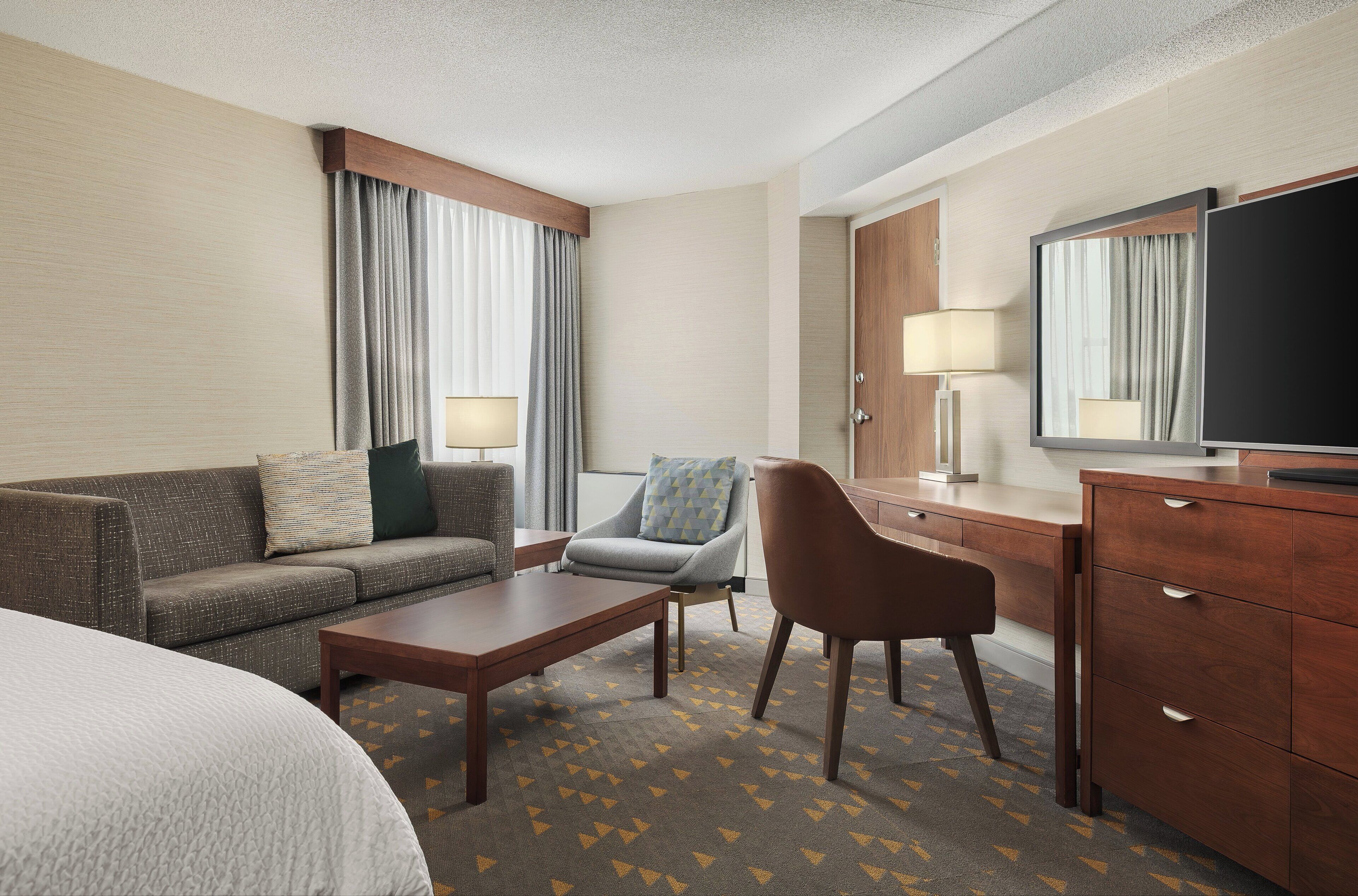A hotel room with a bed, a sofa, a chair, a desk, a television, and a lamp.
