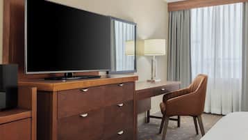 A hotel room with a wooden desk, a television, a chair, and a bed.