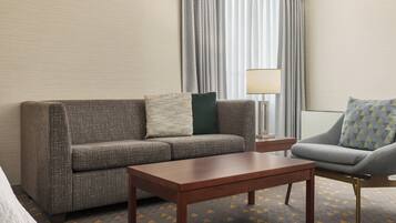A hotel room with a grey sofa, a matching armchair, a wooden coffee table, and a lamp.