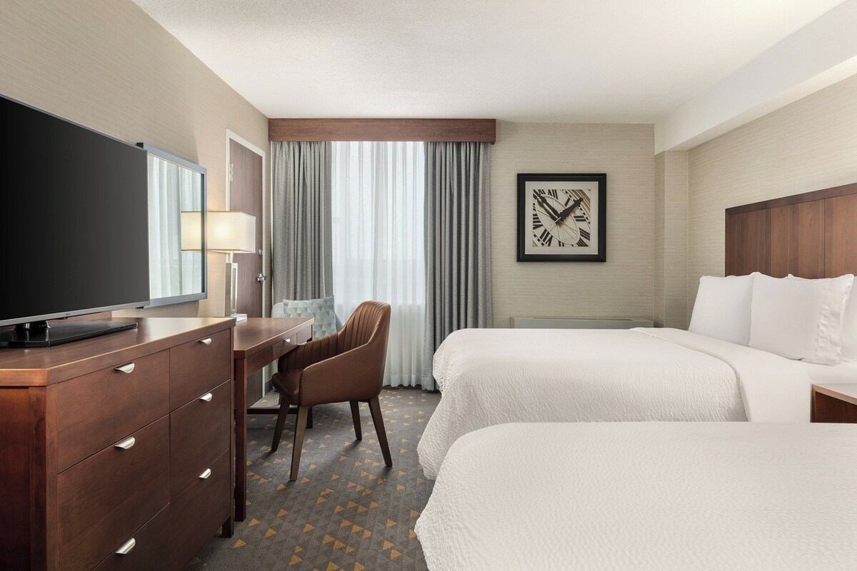 A hotel room with two beds, a desk with a chair, a television, and a framed picture on the wall.