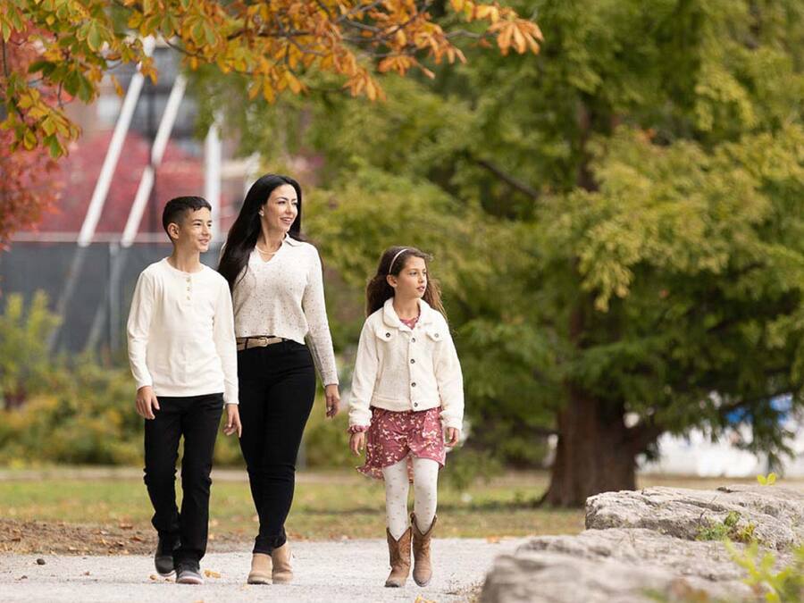 A family walking on a path in a park with trees and a distant building.