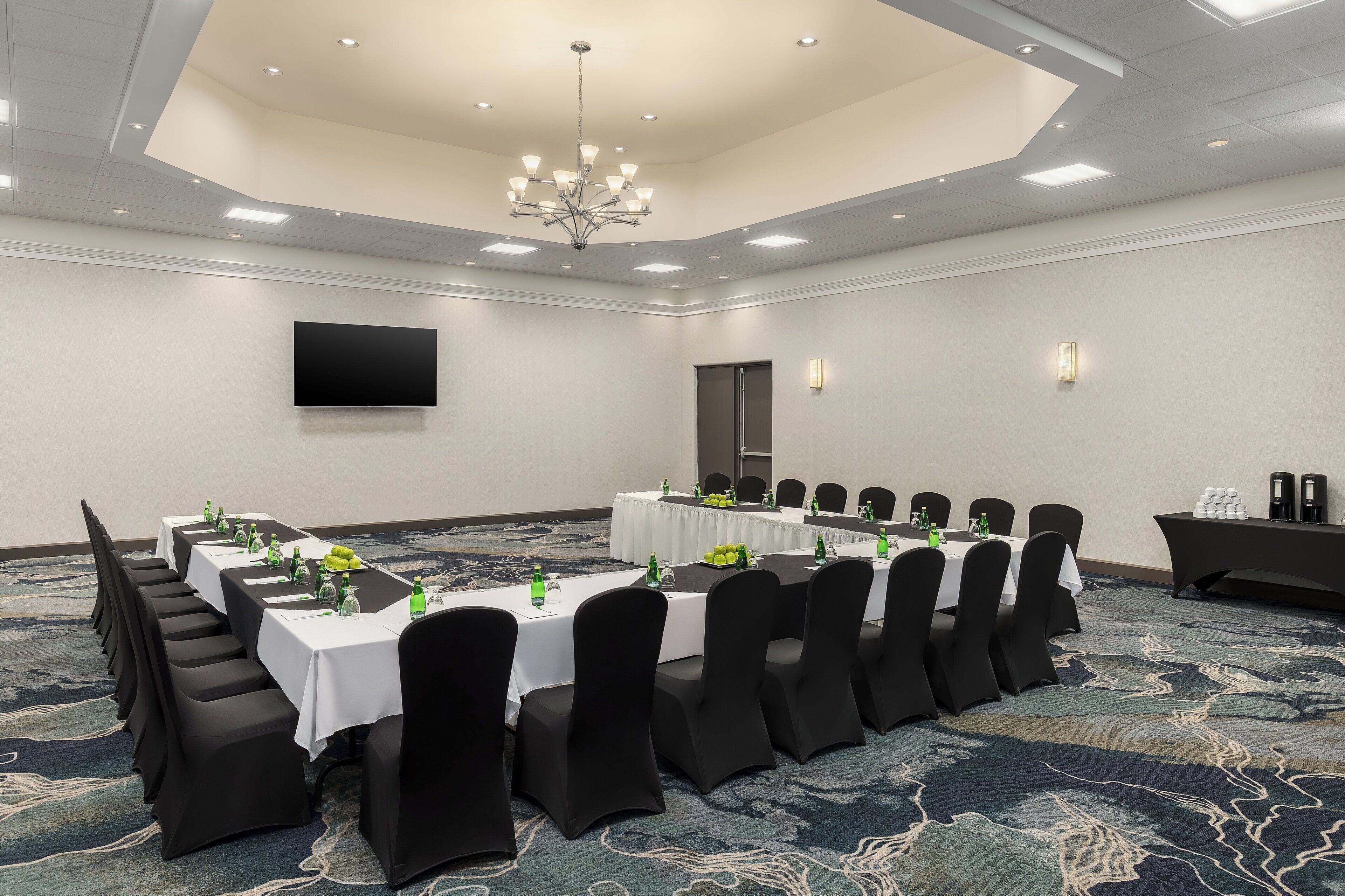 A conference room with a long table, black chairs, and a chandelier.