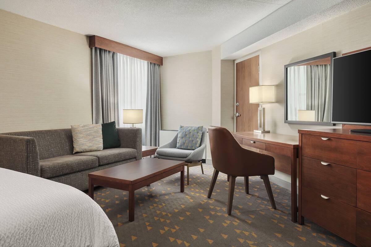 Une chambre d’hôtel comprenant un lit, un canapé, une table basse, un bureau avec une télévision et une chaise.