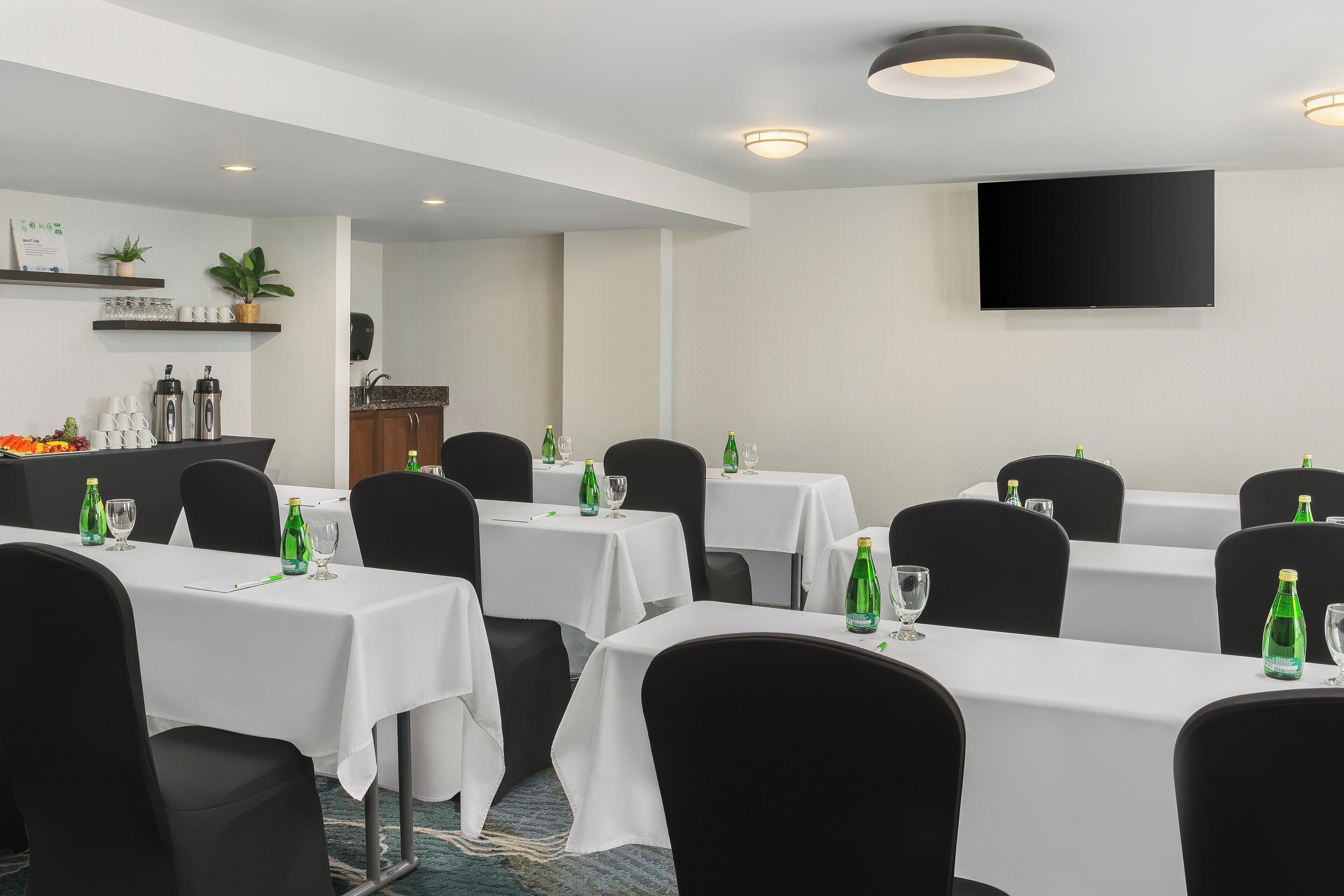 A conference room with multiple tables, chairs, and a flat-screen TV on the wall.