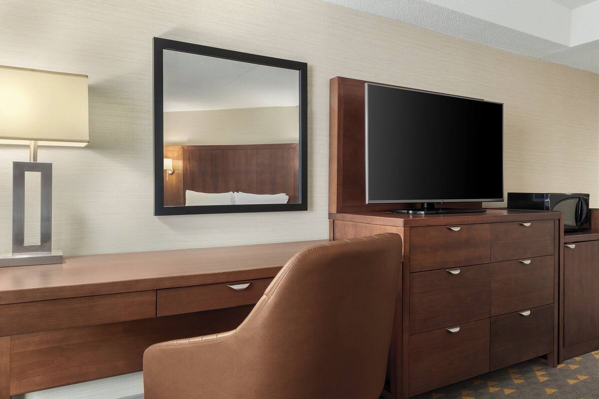 Une chambre d’hôtel avec un bureau en bois, une télévision, un miroir et un fauteuil en cuir.