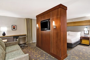 A hotel room with a bed, a desk with a chair, a television, and a lamp.
