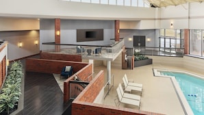 An indoor swimming pool with a sunroof, a seating area with chairs, and a fireplace.