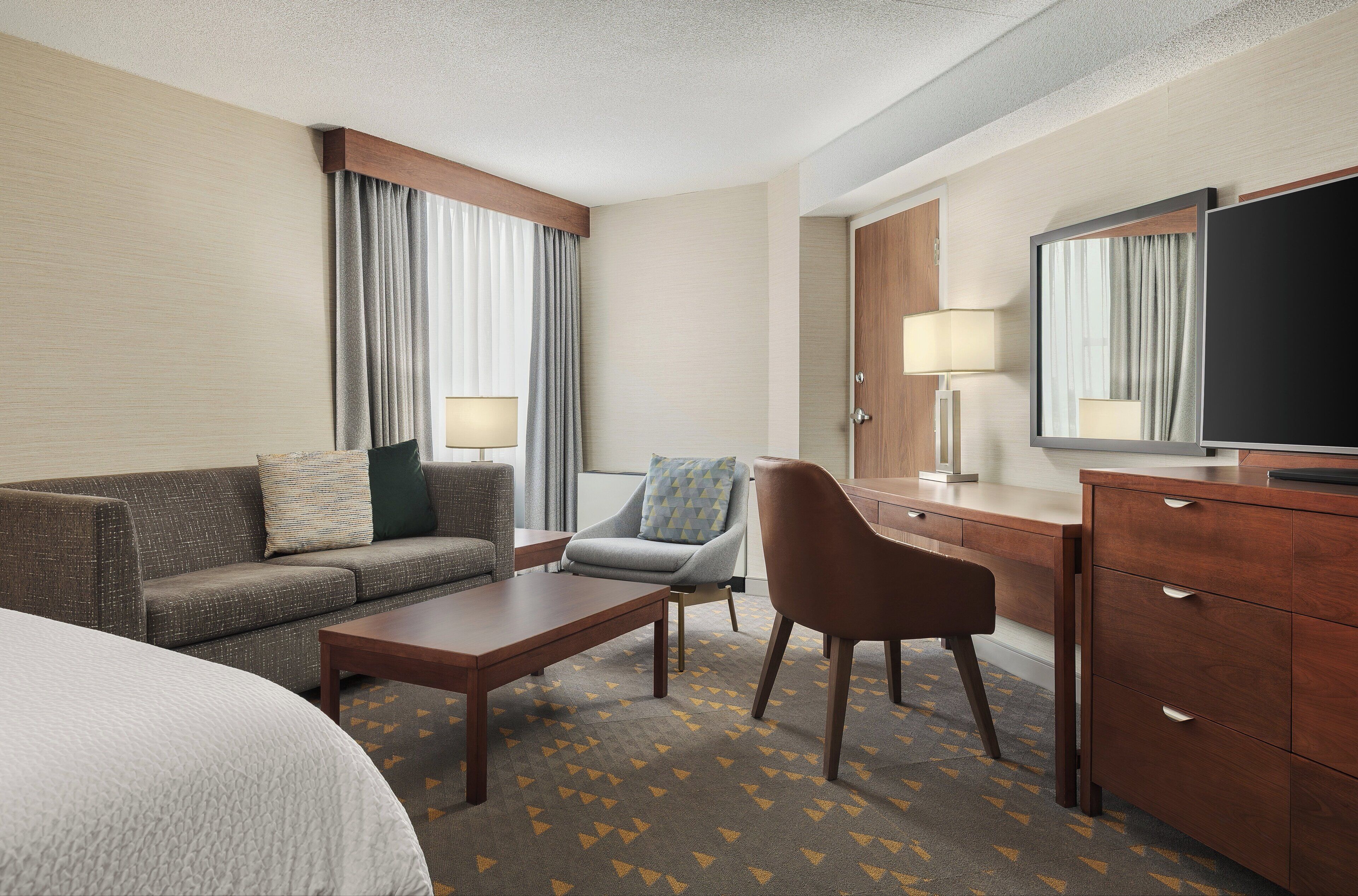 A hotel room with a bed, a sofa, a coffee table, a desk with a TV, and a chair.