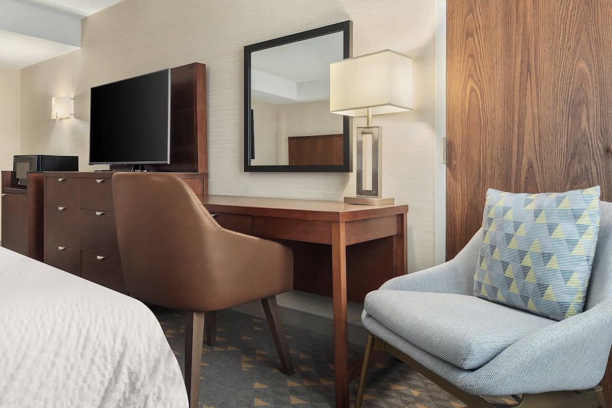 Une chambre d’hôtel comprenant un lit, un bureau avec une télévision, une chaise, une lampe et un panneau en bois.