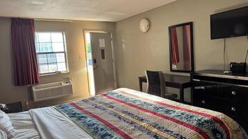 Una habitación de hotel con cama, escritorio, silla, televisor y ventana con cortinas.