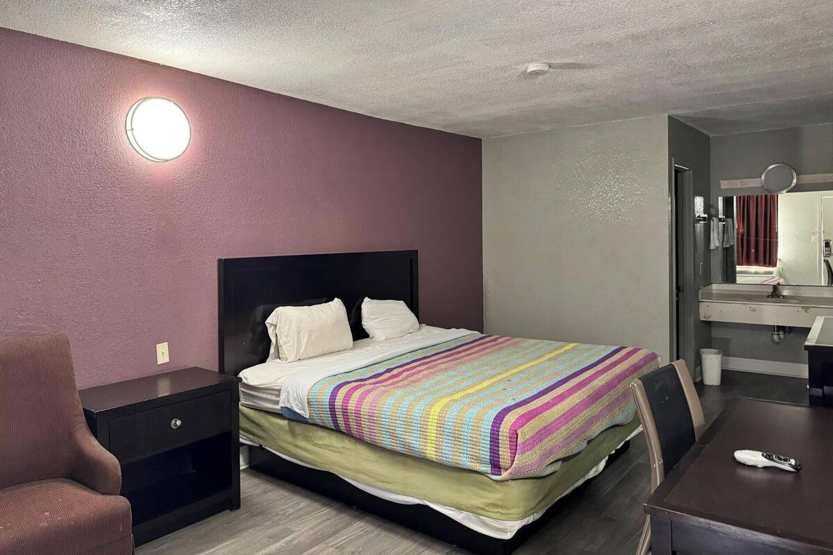 A hotel room with a bed, bedside table, chair, and a small desk with a mirror.