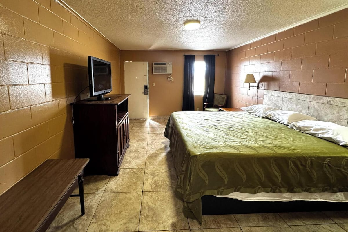 A hotel room with a bed, a TV, a desk, a lamp, and a door.