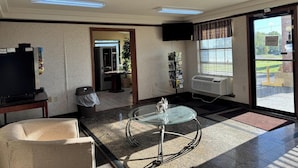 A hotel lobby with a glass table, a sofa, a TV, a trash bin, a bulletin board, and a large window. - Diamond Inn Forrest City I-40 (Forrest City)