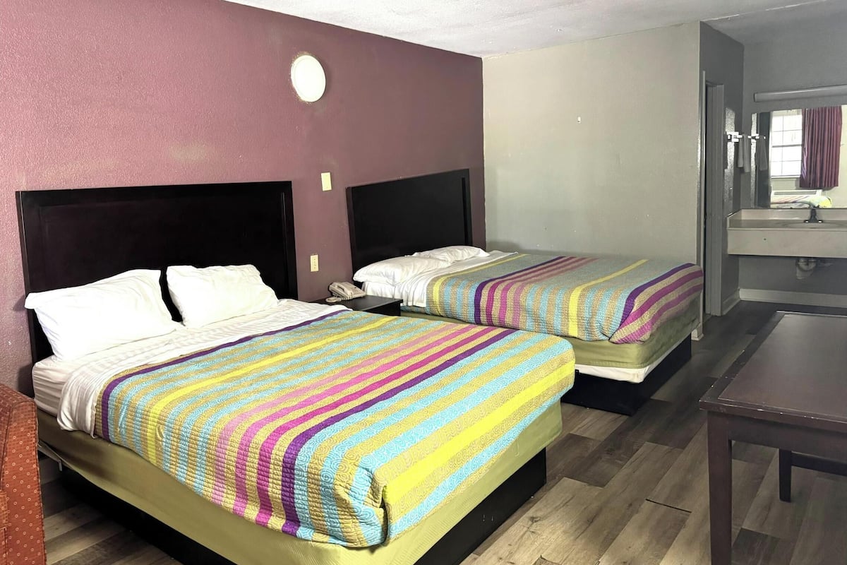 Two beds with striped bedding, a round light fixture on the wall, and a bathroom with a mirror and sink.