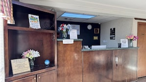 A hotel reception desk with a wooden counter, a vase of flowers, and various signs including one for a nearby McDonald's. - Diamond Inn Forrest City I-40 (Forrest City)
