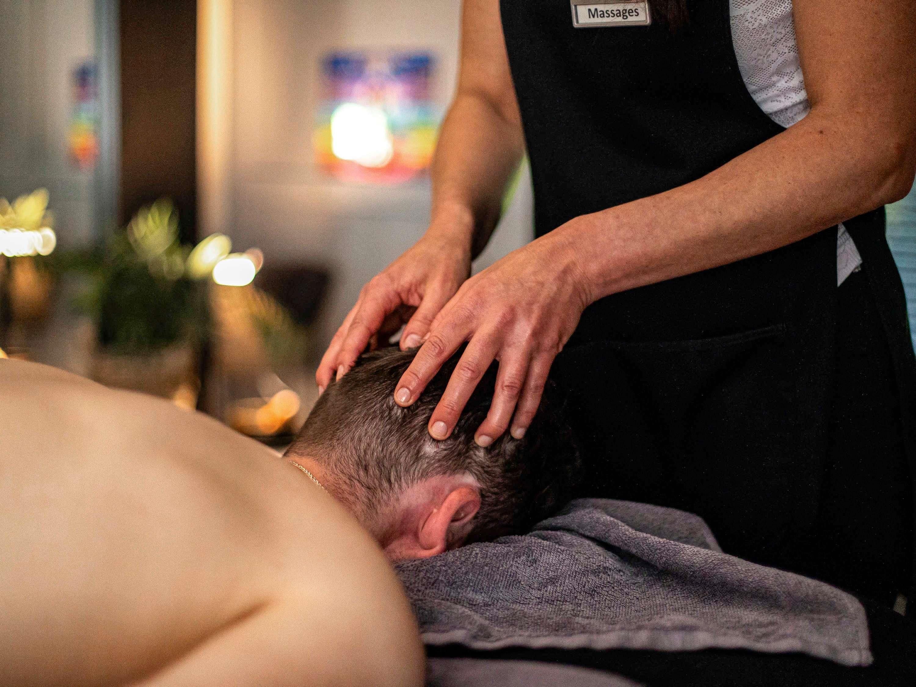 A massage therapy session in progress with a therapist's hands on a client's head.