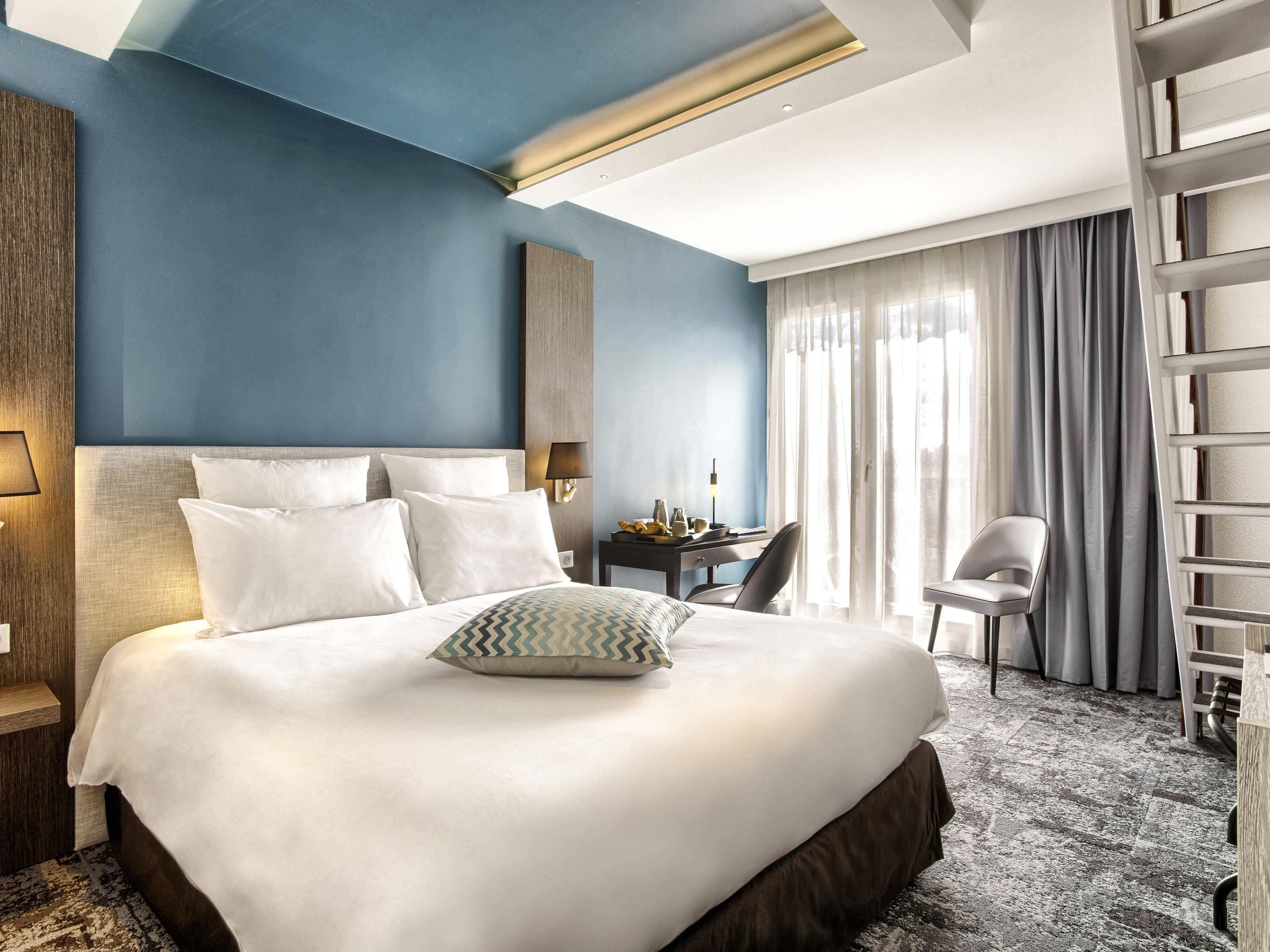 Une chambre d’hôtel avec un grand lit, un bureau avec une lampe, une chaise et une armoire.