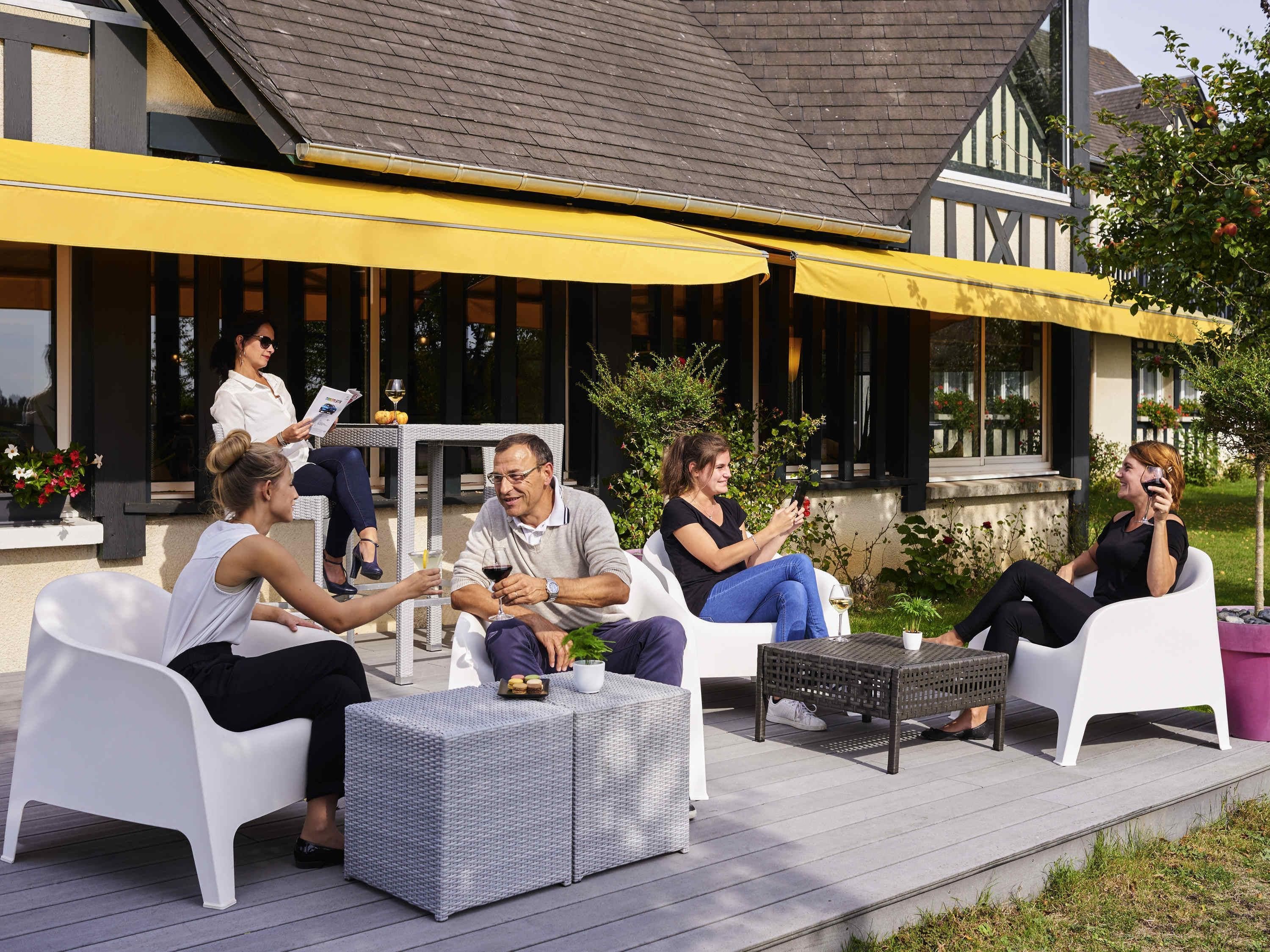 A covered outdoor seating area with white furniture and a yellow awning.