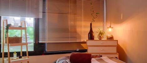 Un dormitorio con cama, mesita de noche, lámpara y ventana con persianas.