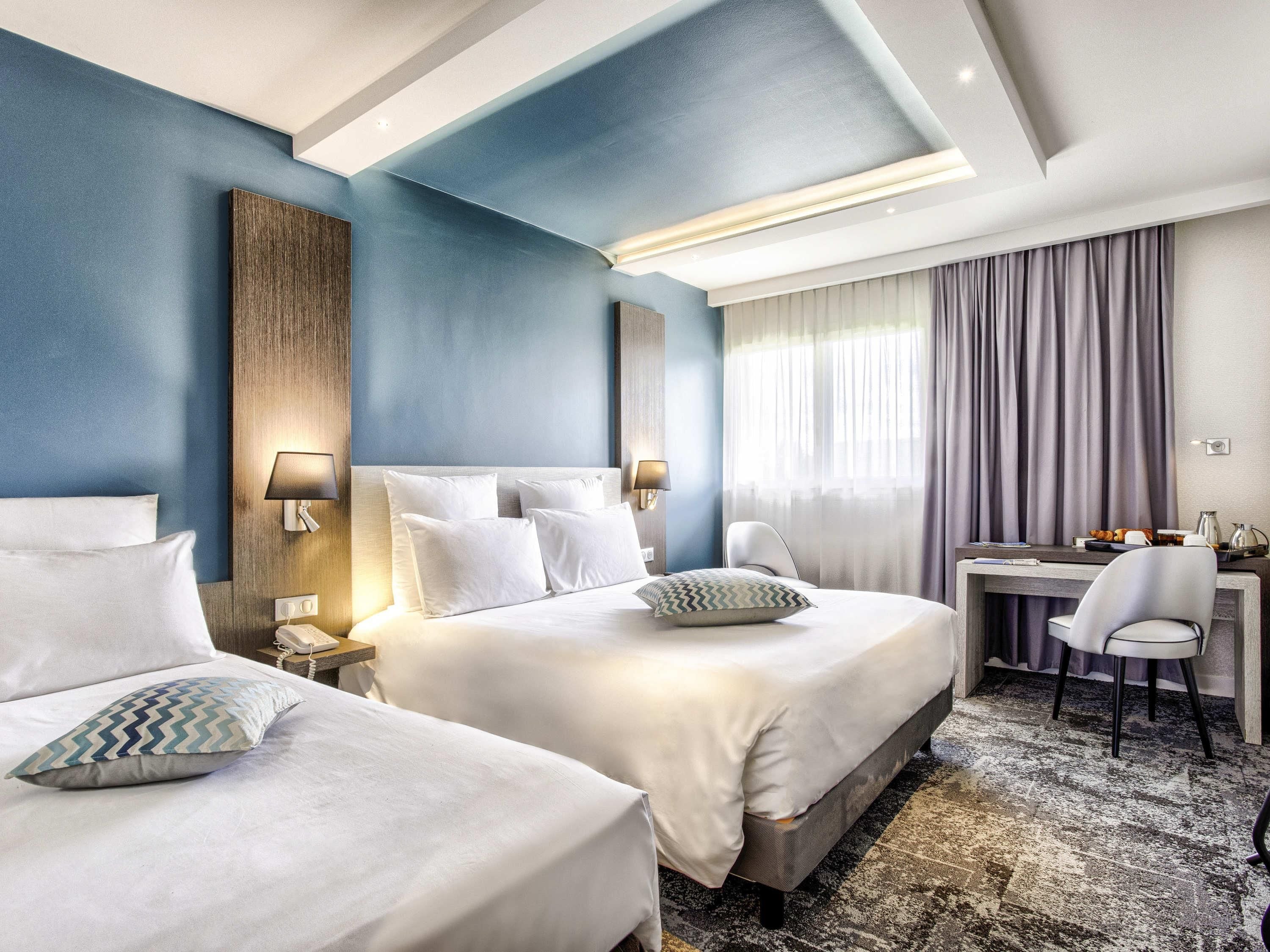 A hotel room with two beds, a desk, and a chair.