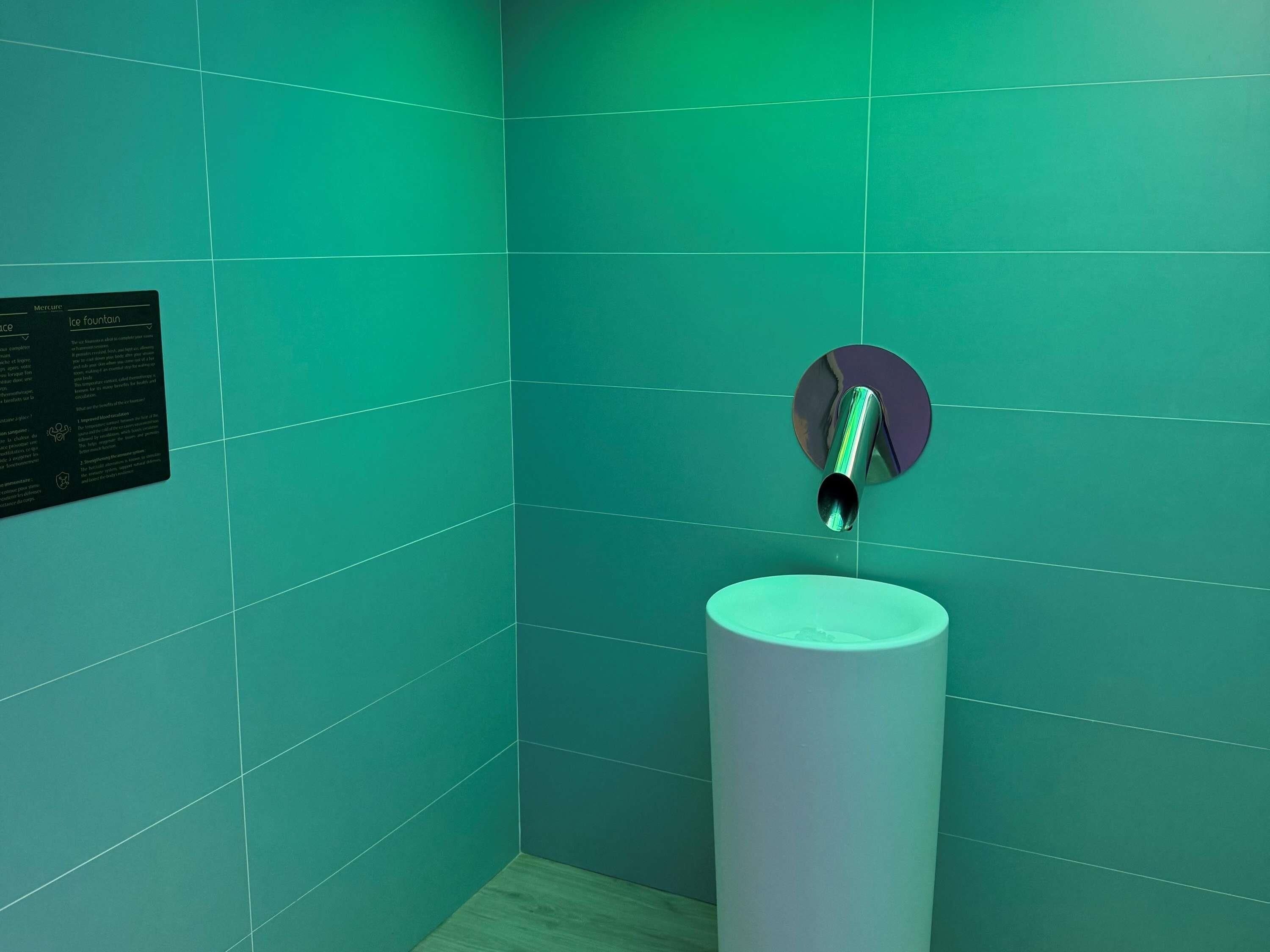 A bathroom with teal tiles, a white sink, and a wall-mounted faucet.