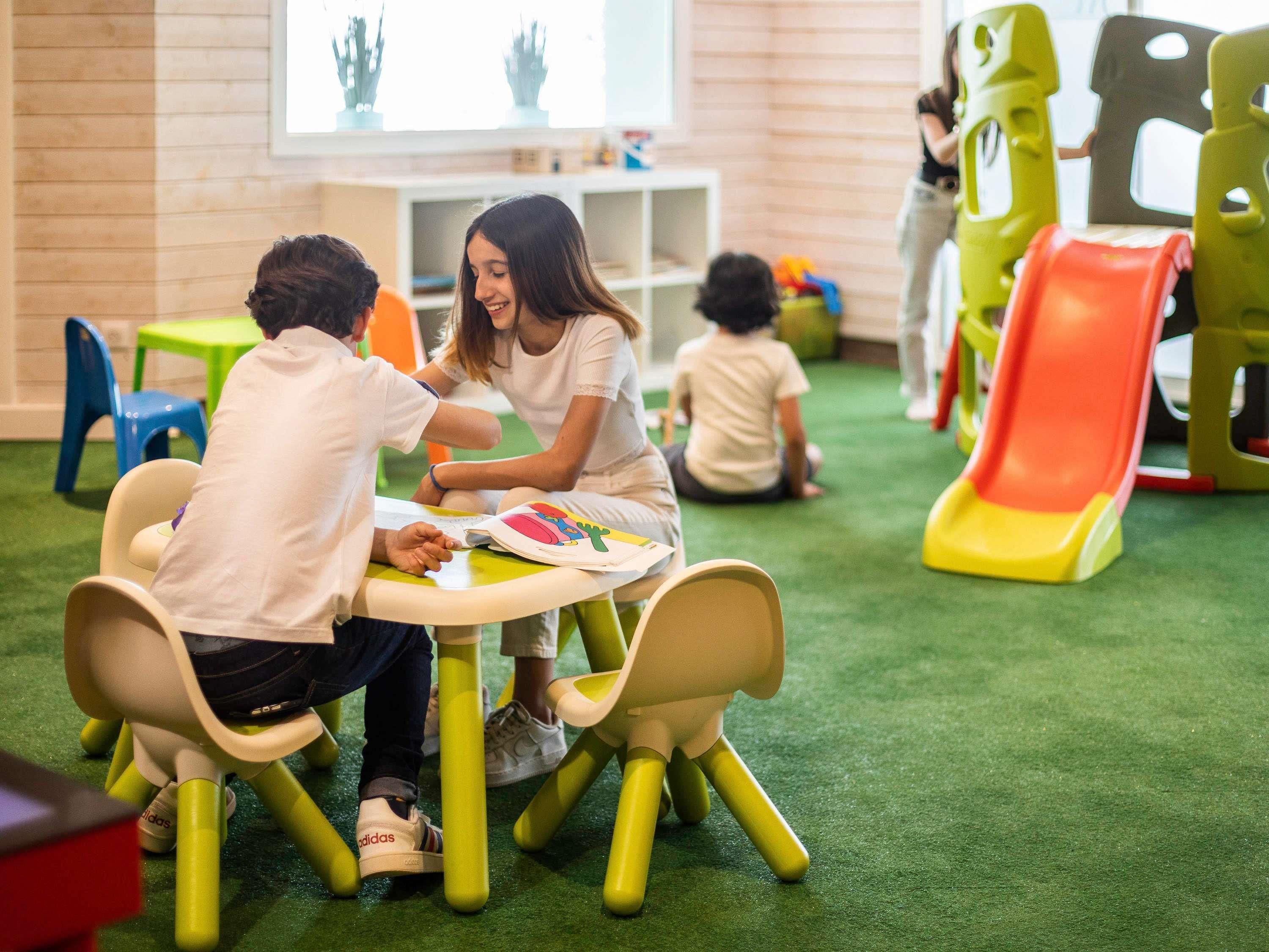 Een groep kinderen die een lesactiviteit doet aan een tafel met een vloerbedekking in groene tinten.