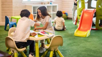 Een groep kinderen die een lesactiviteit doet aan een tafel met een vloerbedekking in groene tinten.