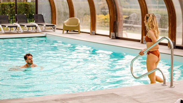 Una piscina interior con techo de cristal, sillas de descanso y vistas al exterior.