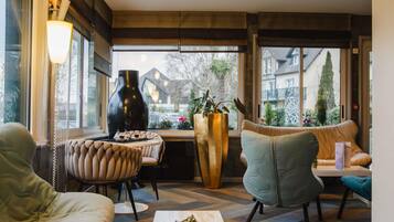 Un intérieur moderne avec un canapé, des fauteuils, une table et une grande fenêtre donnant sur des immeubles et des arbres.