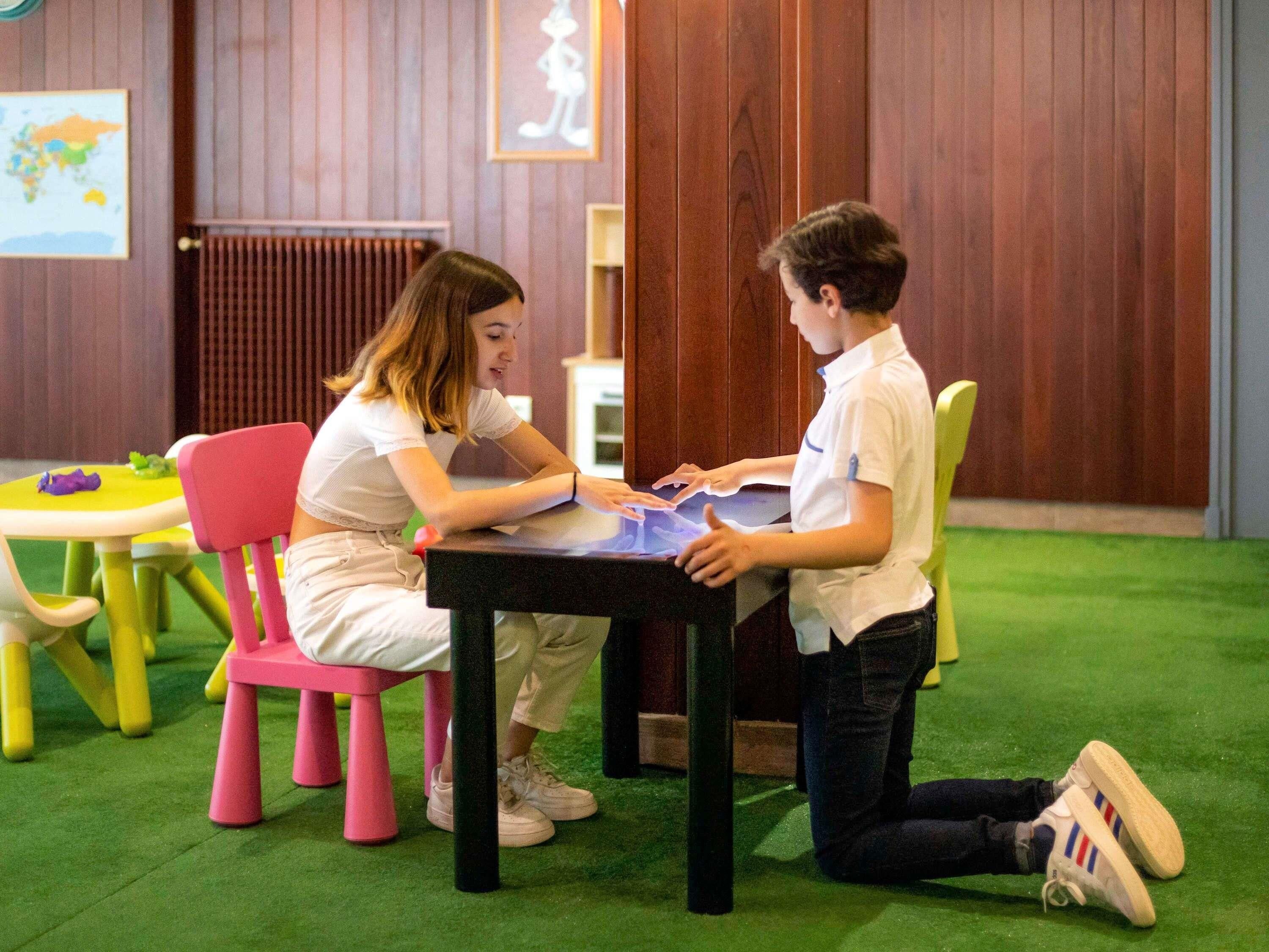 Two individuals seated at a table with a map and papers, in a room with wooden walls and a green carpet.