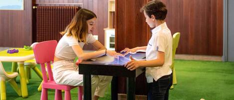 Two individuals seated at a table with a map and papers, in a room with wooden walls and a green carpet.