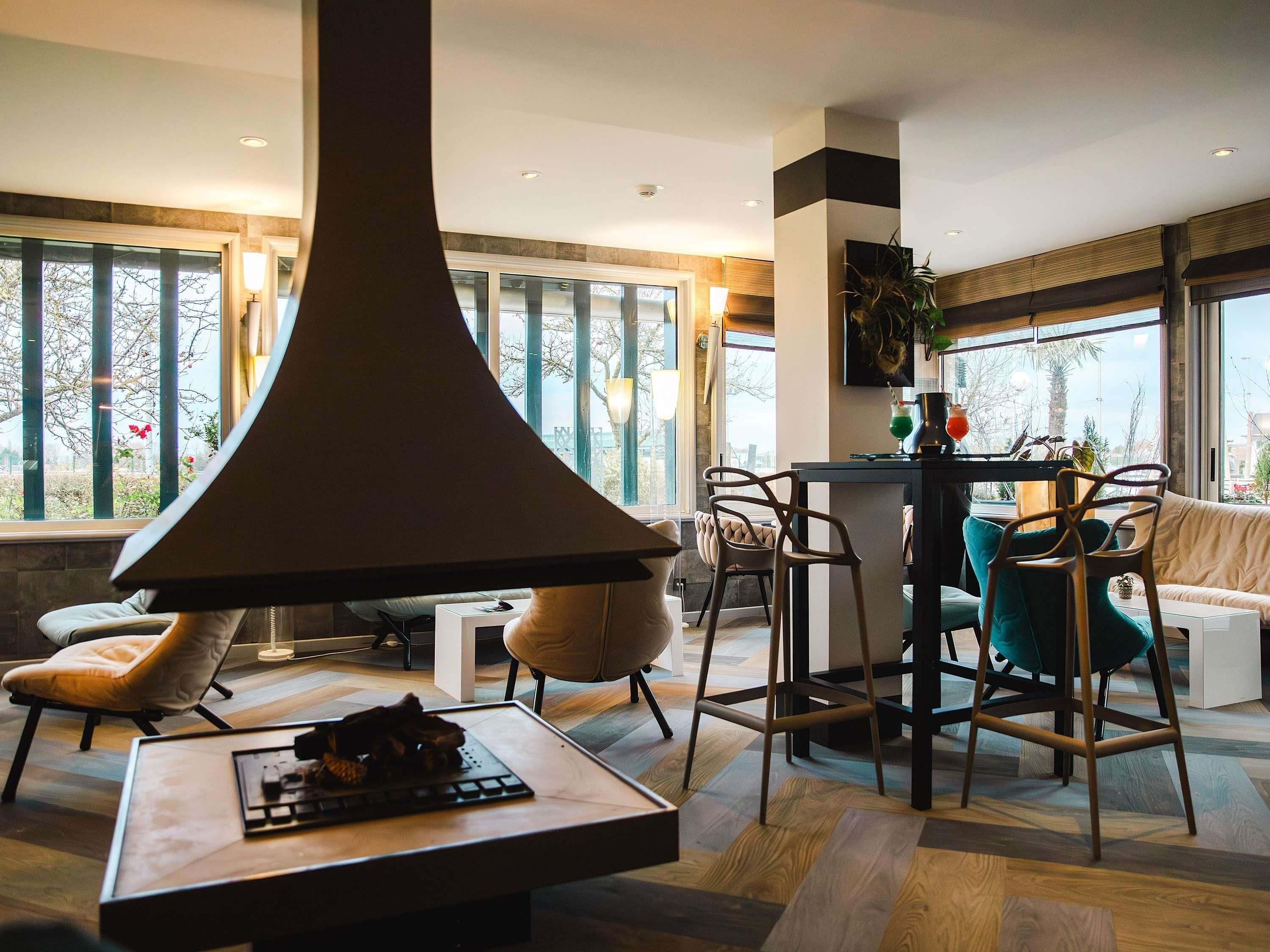 Un salon moderne doté d’une grande fenêtre, d’un luminaire suspendu original, d’un coin repas avec des tabourets de bar et d’un espace salon confortable.