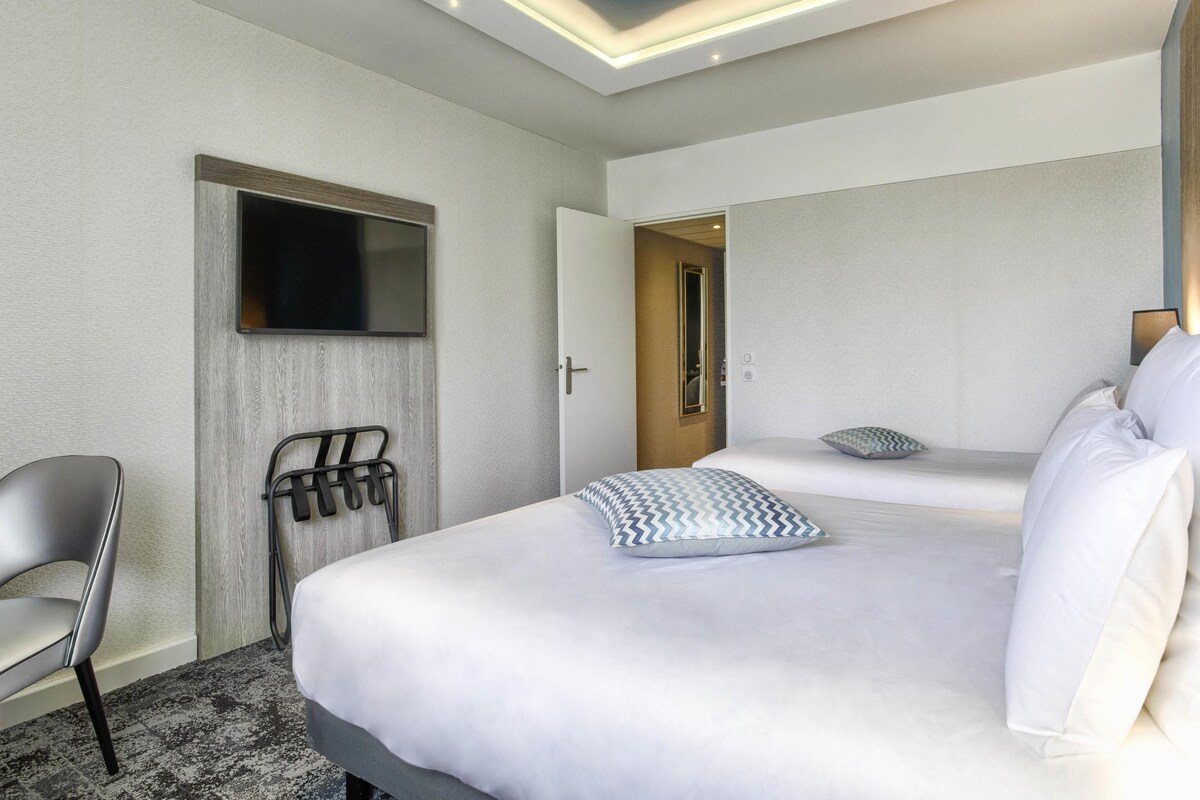 A hotel room with a bed, a chair, a TV, and a door leading to another room.