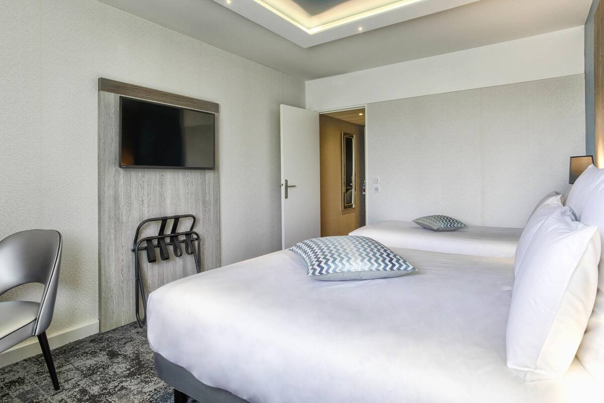 A hotel room with a bed, a chair, a TV, and a door leading to another room.