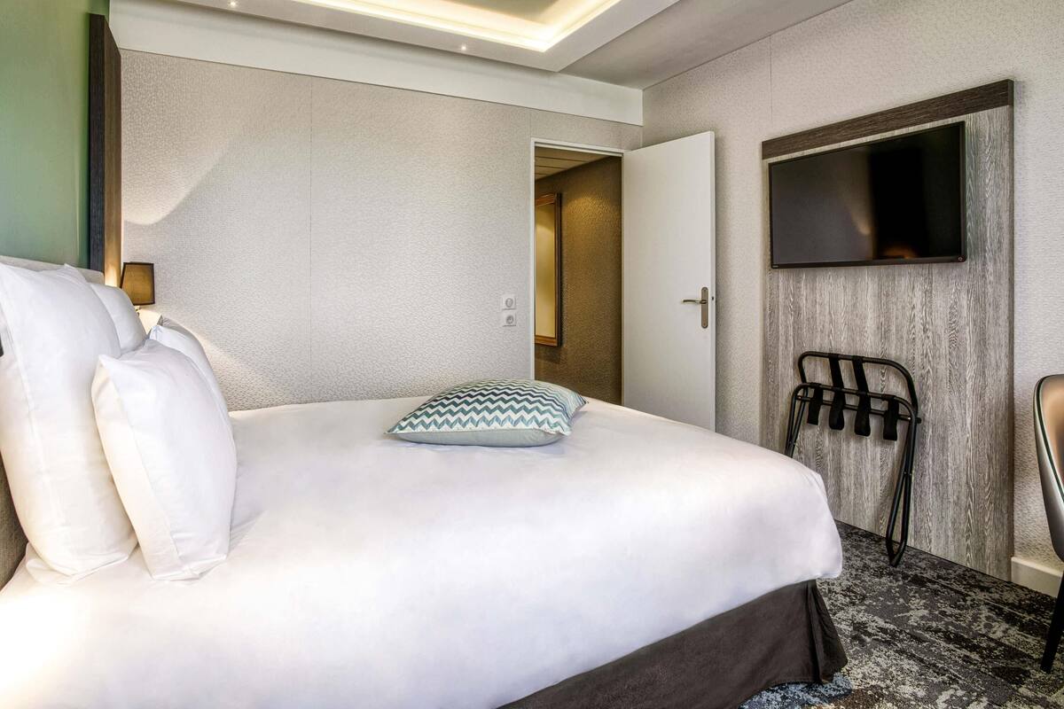 A hotel room with a bed, a TV mounted on the wall, a door, and a coat rack.