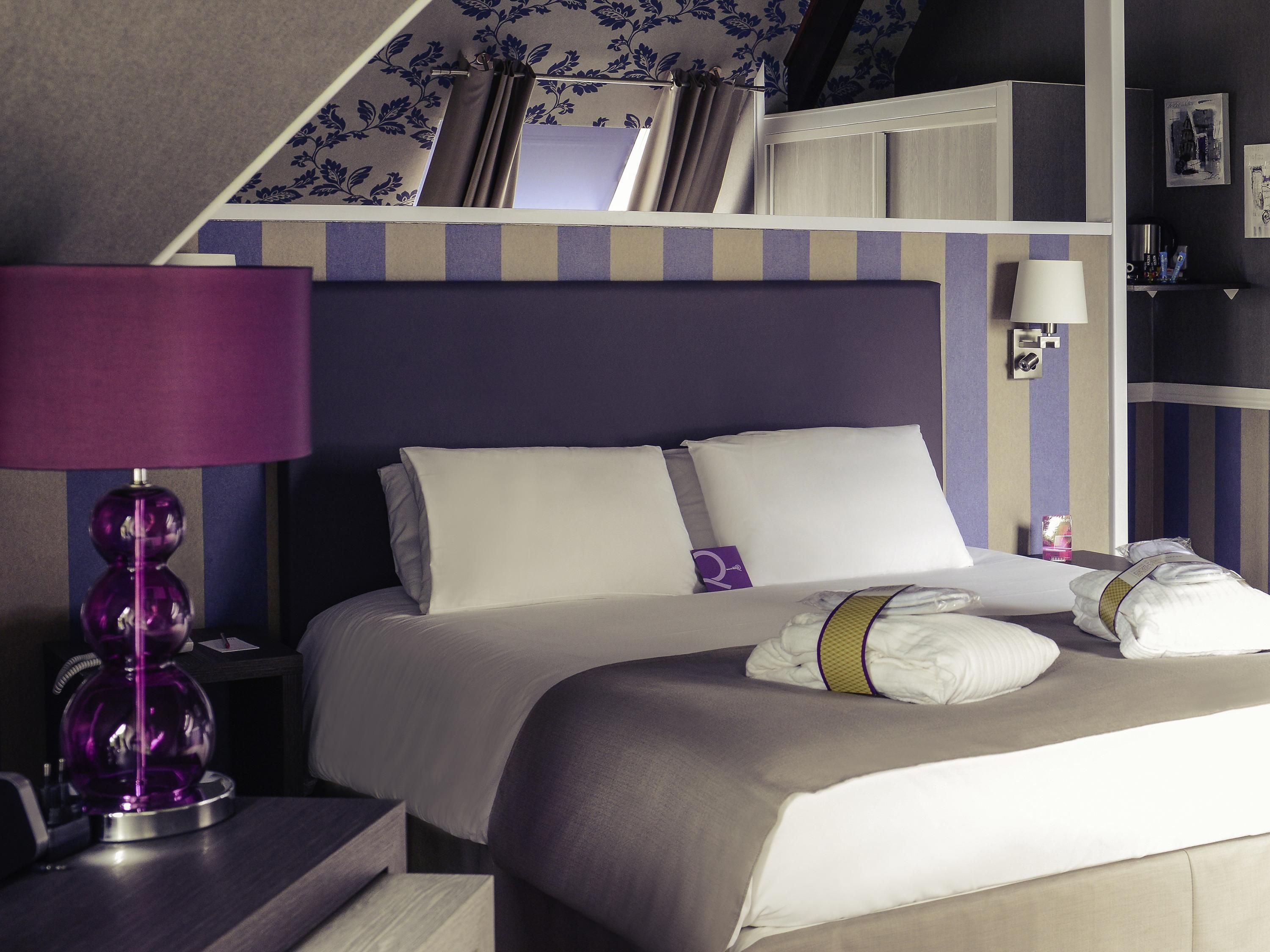 Una habitación de hotel con cama, escritorio, lámpara y estantería.