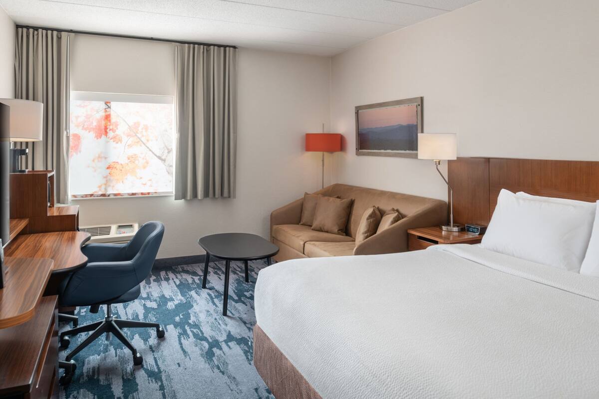 Een hotelkamer met een groot bed, een bureau met stoel, een klein tafeltje, een bank en een raam met gordijnen.