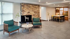A modern living room with a stone fireplace, two green armchairs, a round coffee table, and a dining area with a wooden table and chairs.