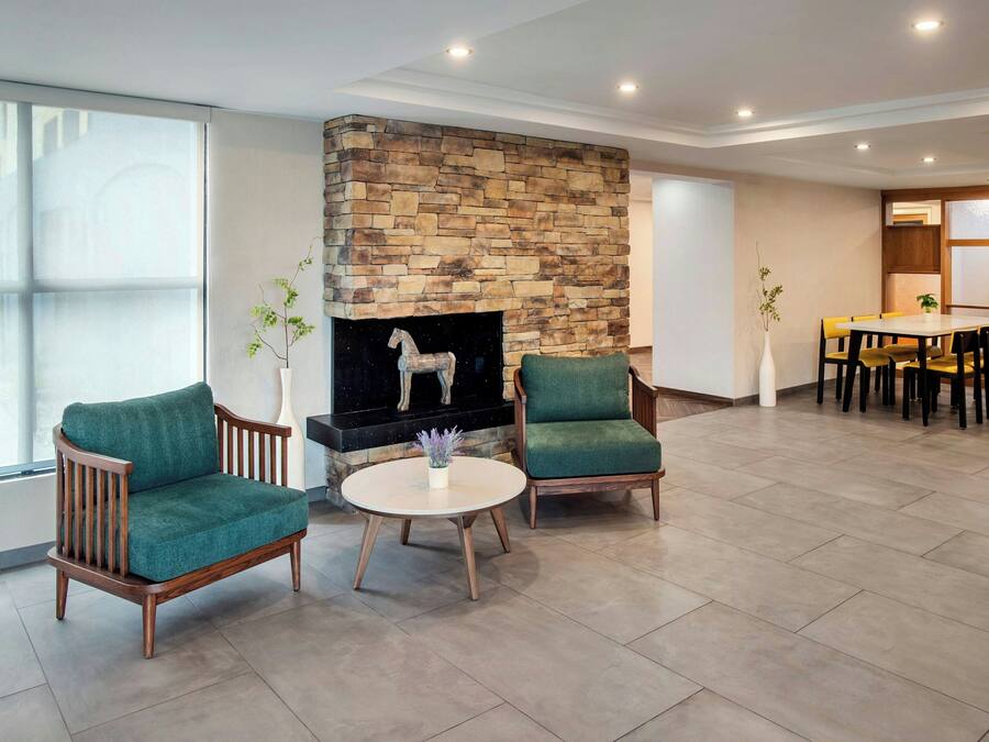 A modern living room with a stone fireplace, two green armchairs, a round coffee table, and a dining area with a wooden table and chairs.