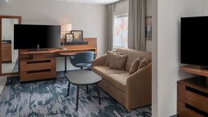 A hotel room with a desk, a sofa, a television, and a window with curtains.