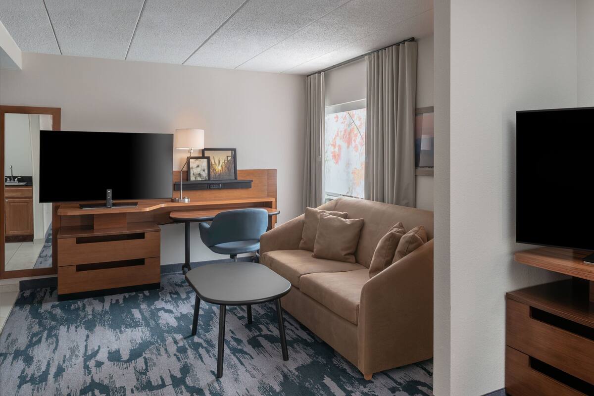 Een hotelkamer met een bureau, een bank, een televisie en een raam met gordijnen.