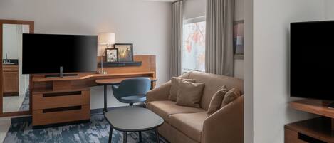 A hotel room with a desk, a sofa, a television, and a window with curtains.