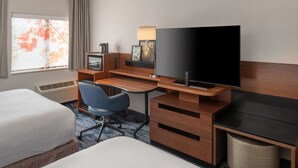 A hotel room with a bed, a desk with a television, a chair, and a window with curtains.