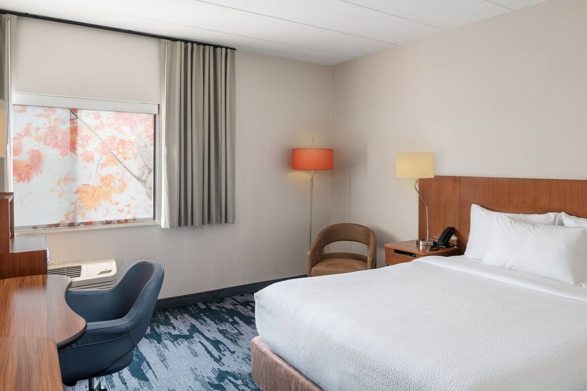 Hotelkamer met een bed, bureau, stoel, lamp en raam met gordijnen.