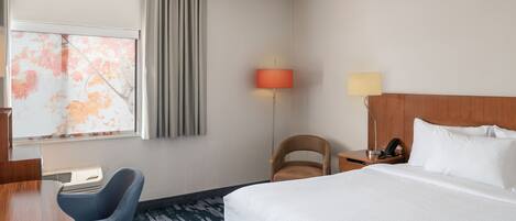 Habitación de hotel con cama, escritorio, silla, lámpara y ventana con cortinas.