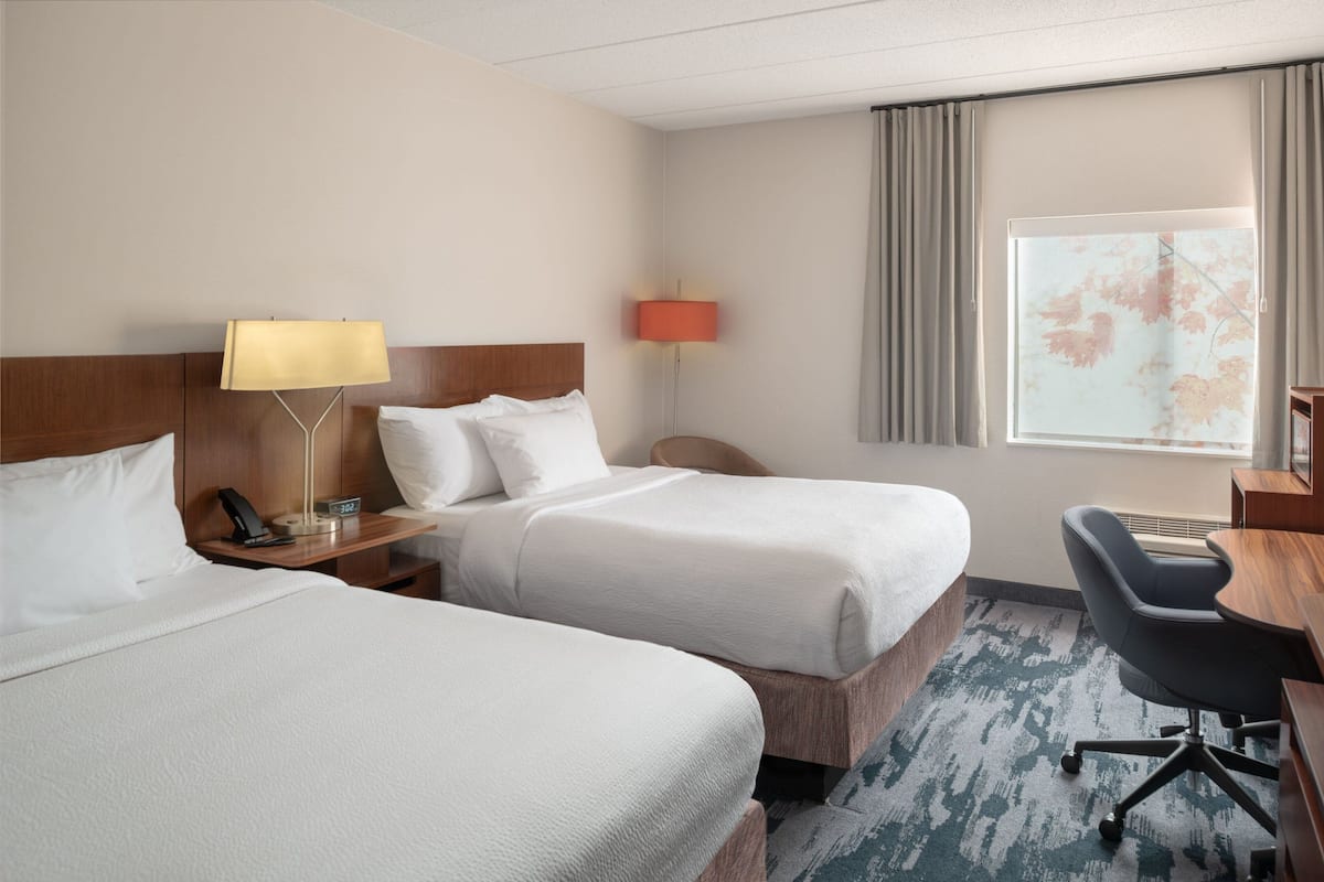 Een hotelkamer met twee bedden, een bureau, een stoel, een lamp en een raam met gordijnen.
