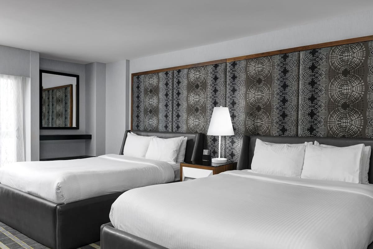 A hotel room with two beds, a large patterned headboard, a nightstand with a lamp, and a mirror on the wall.