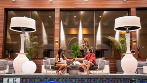 Un espace aménagé au bord de la piscine, avec deux personnes qui discutent, entourés de mobilier moderne et de grandes lampes.