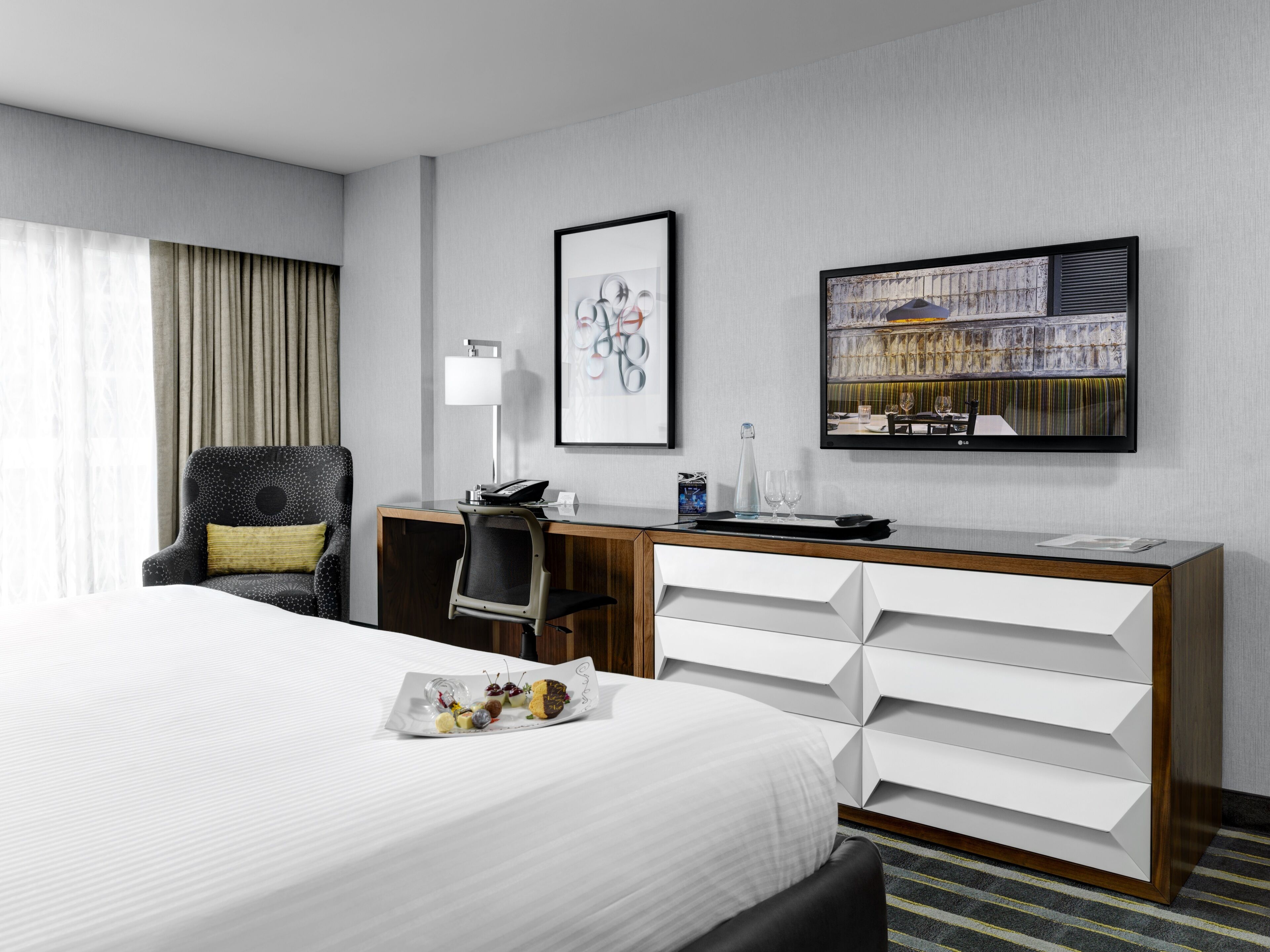Una habitación de hotel moderna con una cama grande, un escritorio con una silla, un televisor de pantalla plana y un cuadro en la pared.